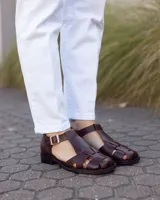 Sandalias estilo romano de cuero marrón oscuro, con diseño de tiras entrelazadas, talón cerrado y hebilla metálica de ajuste lateral.