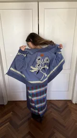 Saco tipo cardigan de punto jacquard color azul, con cierre frontal de aluminio. Presenta un diseño floral en la espalda y detalle de rombos en el ruedo y puños.