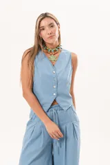 Chaleco de denim fino y liviano color celeste, con silueta entallada, escote en V y cierre frontal con botones de nácar. Presenta un diseño sastrero con terminación en puntas en la delantera.