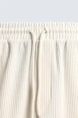 Bermuda de corte relajado, color crema o blanco roto, con textura acanalada (canalé). Presenta cintura elástica ajustable con cordón, bolsillos de vivo frontales y un bolsillo plastrón trasero.