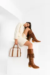 Bota tejana de cuero color marrón, con caña alta con flecos, taco de madera foliado en cuero y cierre lateral.