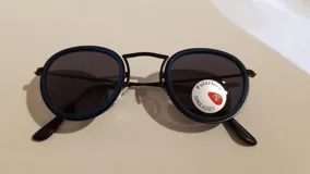 Lentes de sol con montura redonda de metal negro y aro exterior de plástico azul.