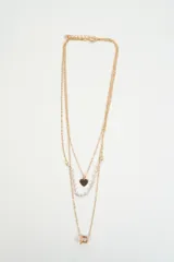 Collar triple de cadena fina dorada. La primera cadena presenta un dije de corazón, la segunda cadena tiene pequeñas perlas blancas y la tercera cadena incluye un dije cuadrado con un cristal central.