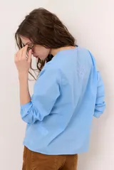 Blusa celeste de manga larga con delicados bordados florales en tono más claro en la zona del pecho y mangas. Presenta escote en V y puños elásticos abotonados.