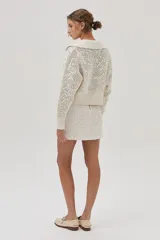 Cárdigan tejido de punto calado color crudo, con cuello polo, cierre metálico frontal y mangas largas.