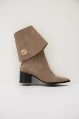 Bota de cuero color chocolate con diseño versátil que incluye una polaina desmontable. Presenta punta fina, taco cuadrado y un detalle bordado en la parte superior de la caña.