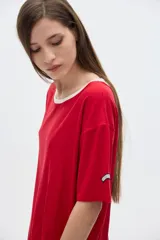 Remera oversized de manga corta en tejido rib blanco, con cuello redondo amplio ribeteado en negro. Presenta un pequeño parche rectangular con texto en la manga izquierda.