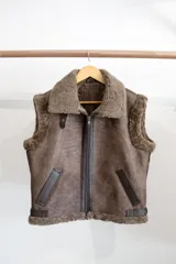 Chaleco estilo bomber de cuero negro con interior y detalles de piel sintética en color crema. Presenta cierre frontal con solapa de cuero en tono tostado y mangas de tejido de punto color crema.