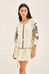 Vestido corto de bambula color celeste, con escote redondo, mangas tres cuartos abullonadas y falda con volado en el ruedo. Presenta bordados decorativos en el frente y las mangas, y cuenta con un cinturón de la misma tela para ajustar a la cintura.