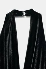 Vestido corto de terciopelo negro con cuello halter, escote en pico pronunciado y espalda descubierta. Presenta un detalle de nudo delantero con flecos largos y cierre de cremallera oculta.