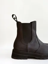 Bota tipo Chelsea de caña media, confeccionada en cuero negro con acabado mate. Presenta paneles elásticos laterales, tiradores traseros y suela track robusta con plataforma dentada.