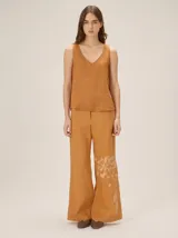 Pantalón de lino color mostaza, de corte recto y amplio, con estampa botánica en tono más claro en la parte inferior de una de las piernas.