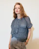 Remera blanca de lino con cuello mao, media cartera con broches metálicos y manga japonesa. Presenta un bolsillo frontal tipo plaqué, recortes laterales en sisa con detalles de encaje y ruedo redondeado con corte escalonado.