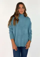 Sweater de punto color azul, con cuello alto, mangas largas y diseño holgado con puños y ruedo acanalados.