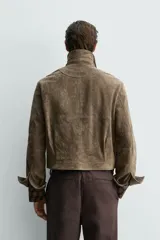 Cazadora de corte boxy fit confeccionada en piel con acabado de ante. Presenta cuello solapa, cierre frontal con cremallera, mangas largas con puños ajustables mediante botón a presión oculto y dos bolsillos de plastrón con solapa en la parte frontal.