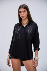 Camisa negra de manga larga con detalles de lentejuelas y bordados en el pecho, cuello camisero y cierre de botones.