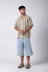 Camisa de manga corta con cuello clásico y cierre frontal de botones. Confeccionada en tejido de punto crochet calado, presenta un patrón de rayas verticales negras sobre fondo crudo.