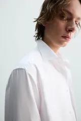 Camisa blanca de corte slim fit, confeccionada en tejido de algodón. Presenta cuello italiano, manga larga con puño abotonado y cierre frontal de botonadura.