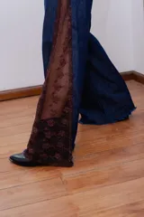 Pantalón de jean estilo wide leg, confeccionado en denim rígido de color azul oscuro. Presenta paneles laterales de encaje con diseño floral en tono rojizo y terminaciones deshilachadas en el ruedo.