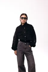 Campera de jean negra con mangas largas tejidas en crochet con diseño calado y detalles florales en relieve. Presenta cuello camisero, cierre frontal y bolsillos en el pecho.