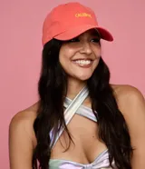 Gorra de sarga color salmón, con visera curva y el texto "CALIENTE" bordado en hilo amarillo en el frente.