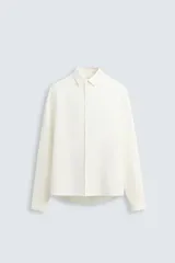 Camisa de corte relajado confeccionada en tejido de cáñamo, color blanco. Presenta cuello de solapa, manga larga con puños abotonados y cierre frontal de botonadura.