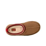 Pantuflas tipo mule UGG modelo Tazz II, confeccionadas en gamuza color tostado con plataforma alta. Presentan un detalle de costura trenzada decorativa en el borde superior en tonos rojo y beige, y el logo de la marca grabado en el lateral.