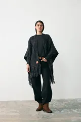 Ruana tejida artesanalmente en lana, con diseño de textura tramada en tonos oscuros con detalles en colores tierra. Presenta un cuello alto y mangas integradas de punto liso.