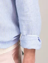 Camisa celeste a rayas verticales de lino, corte regular fit, cuello italiano, cierre con botones, manga larga terminada en puño simple y logo bordado en el pecho.