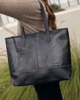 Bolso tipo tote de cuero negro con textura de reptil en la parte superior y base de cuero liso. Cuenta con doble asa de hombro.