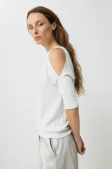 Sweater de tejido de punto fino con efecto lurex brillante, color plateado claro. Presenta un escote bote y aberturas en los hombros (cold shoulder) con mangas tres cuartos.