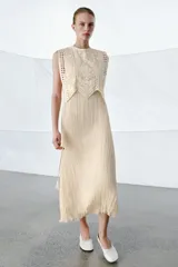 Vestido midi de viscosa con efecto arrugado, cuello redondo y diseño sin mangas. Presenta una sobrecapa superior con bordados detallados y entredoses, con cordones laterales ajustables terminados en borlas.