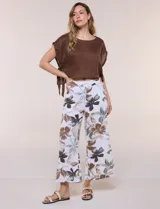 Pantalón crop de lino y rayón, con diseño wide leg de corte holgado, estampado tropical de hojas en tonos verde, azul y marrón sobre fondo blanco. Cuenta con pretina trasera elastizada y bolsillos delanteros.