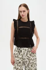 Blusa de algodón negra sin mangas, con cuello a la base, volados en los hombros y detalles de encaje y calados frontales.