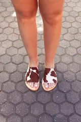 Sandalias bajas de cuero con estampado de vaca en marrón y blanco.