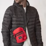 Morral pequeño de diseño técnico en color rojo, con cierre frontal y etiqueta de marca cosida. Cuenta con correa ajustable para llevar cruzado al hombro.