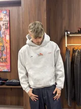 Buzo con capucha gris jaspeado, de corte holgado, con estampado gráfico en la espalda que incluye el texto 'Ittai Company' y una figura de un animal en color rojo.