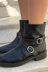 Bota corta de cuero charolado color bordó, con suela track negra, cierre lateral y tiras decorativas con hebillas metálicas plateadas.