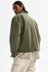 Campera de algodón en color verde militar, con cuello camisero, cierre frontal, un bolsillo superior con cierre y dos bolsillos laterales ribeteados.