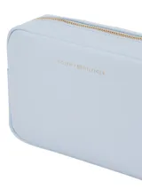 Cartera bandolera rectangular color celeste claro, con acabado liso y logo metálico de Tommy Hilfiger en el frente. Posee un asa ancha tejida con rayas celestes y blancas.