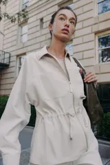 Chaqueta color tostado con cuello solapa, manga larga y cierre frontal con cremallera. Presenta bolsillos delanteros de plastrón con solapa y detalle de cintura ajustable con lazada.