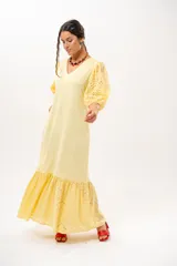 Vestido largo amarillo mantequilla con escote en V, mangas abullonadas y volados en el bajo con detalles de broderie.