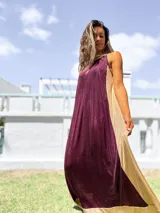 Vestido largo de fiesta con diseño bicolor, presentando un panel frontal en color bordó y paneles laterales en color dorado. Confeccionado en tela brillante con caída fluida, presenta escote halter y corte holgado.