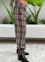 Pantalón de tiro alto con diseño a cuadros en tonos marrón y blanco. Presenta pinzas en la cintura, corte holgado y detalle de ajuste con trabilla en los tobillos.