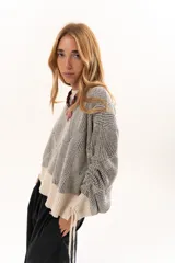 Buzo de tejido de punto con diseño geométrico en relieve, cuello redondo y mangas largas abullonadas con puños ajustables mediante lazos. Presenta un borde inferior en tejido acanalado de color crudo.