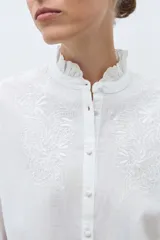 Camisa blanca de manga larga con cuello alto fruncido y bordados calados en el pecho y los hombros.