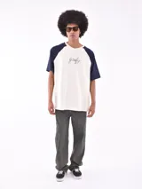 Remera de mangas cortas ranglan, color crudo con mangas azul marino y estampado frontal con la palabra "goofy" en cursiva.