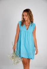 Vestido corto color fucsia, con escote en V profundo y mangas cortas tipo volado. Presenta un diseño con textura de bordado inglés o perforado y un corte imperio con frunce que da volumen a la falda.