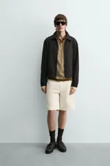 Bermuda de algodón color beige claro, de corte relajado y largo hasta la rodilla. Presenta cierre frontal con cremallera y botón, bolsillos delanteros y bolsillo cerillero, además de bolsillos traseros de plastrón.