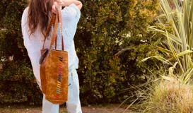 Bolso tote de cuero color marrón con costuras decorativas de hilo de colores.